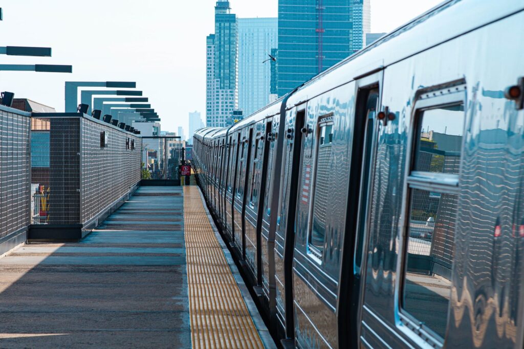 Picture of a stopped train with open doors at a platform, with skyscrapers visible in the distance.